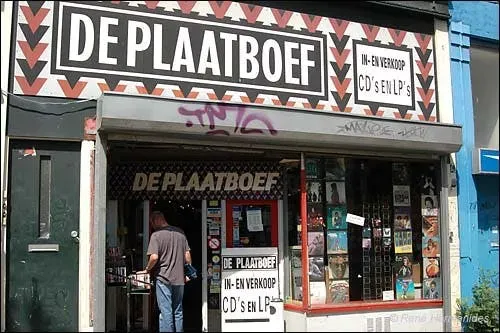 Gevel van De Plaatboef Rotterdam met het zwart-wit-rode uithangbord en een klant die naar binnen loopt.